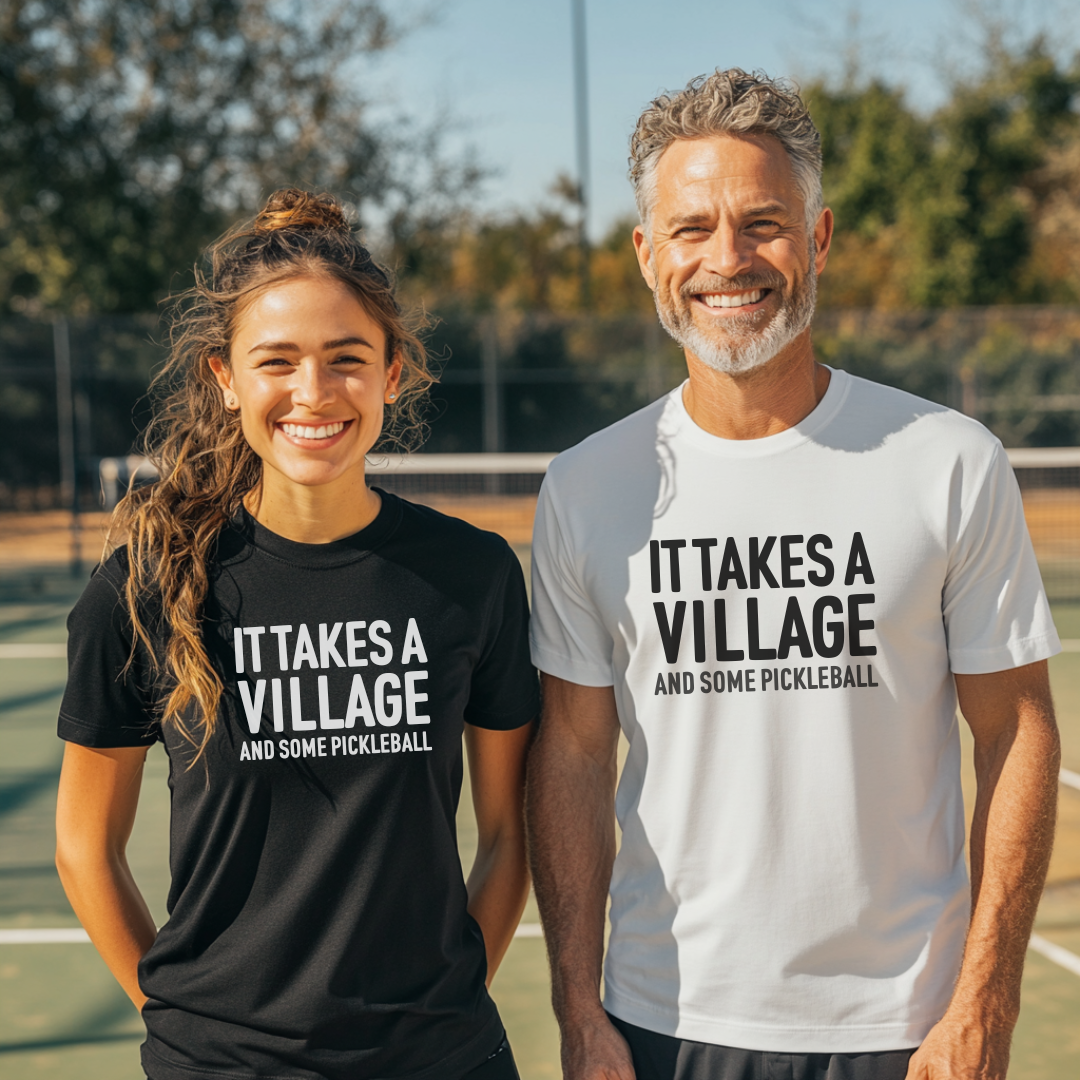 Two people wearing 'It Takes a Village' t-shirts on a pickleball court.